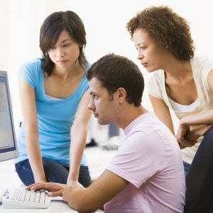 Three people sitting in computer room looking at monitor azienda